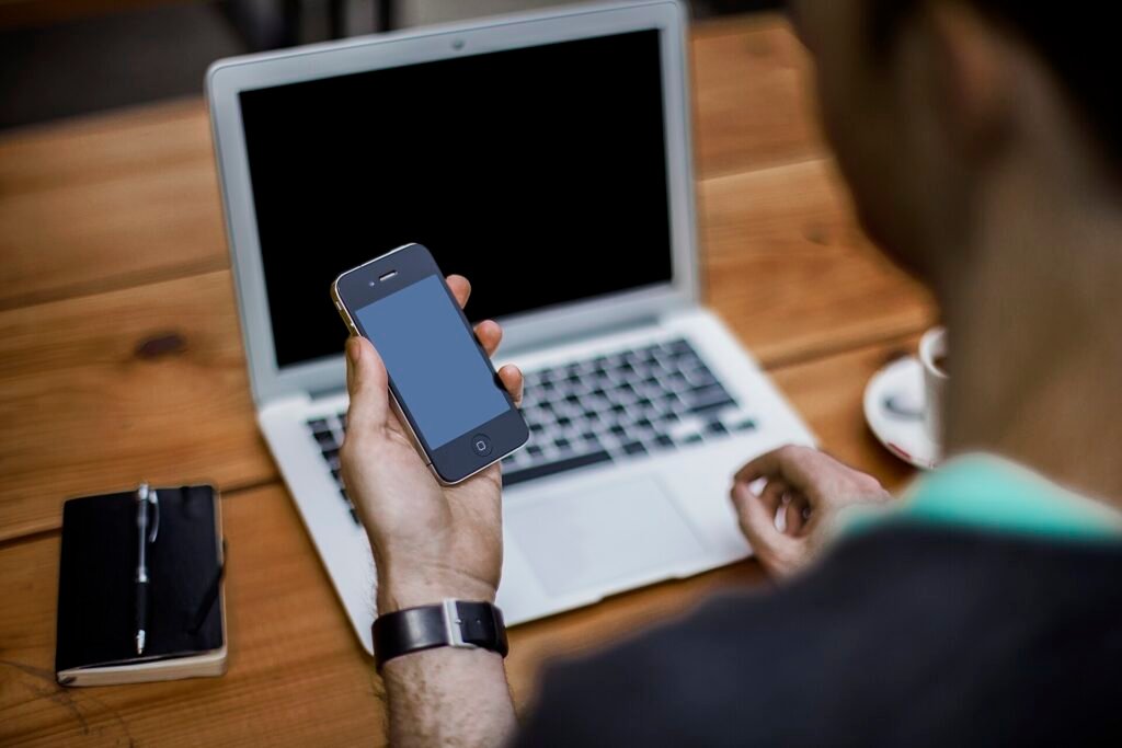 Man using a smartphone next to a laptop