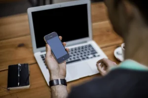Man using a smartphone next to a laptop