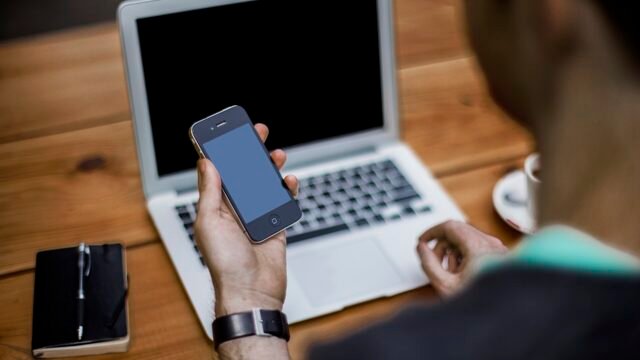 Man using a smartphone next to a laptop