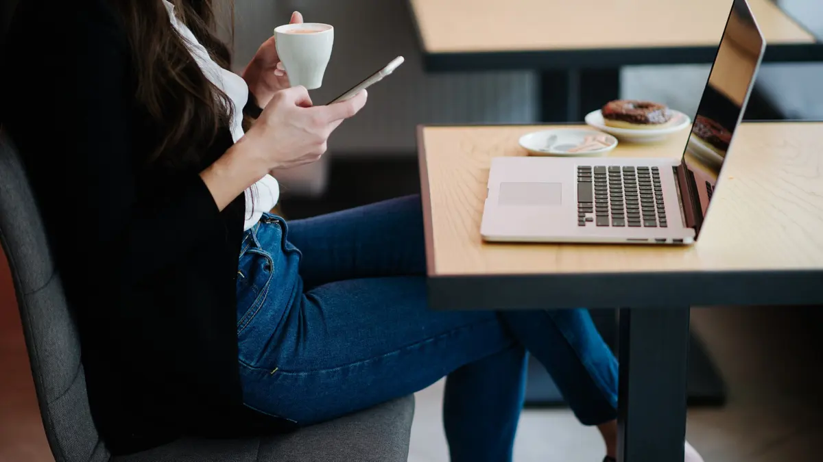 Woman using a smartphone in a cafe with a laptop on the table
