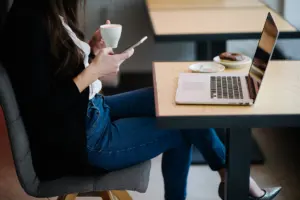 Woman using a smartphone in a cafe with a laptop on the table